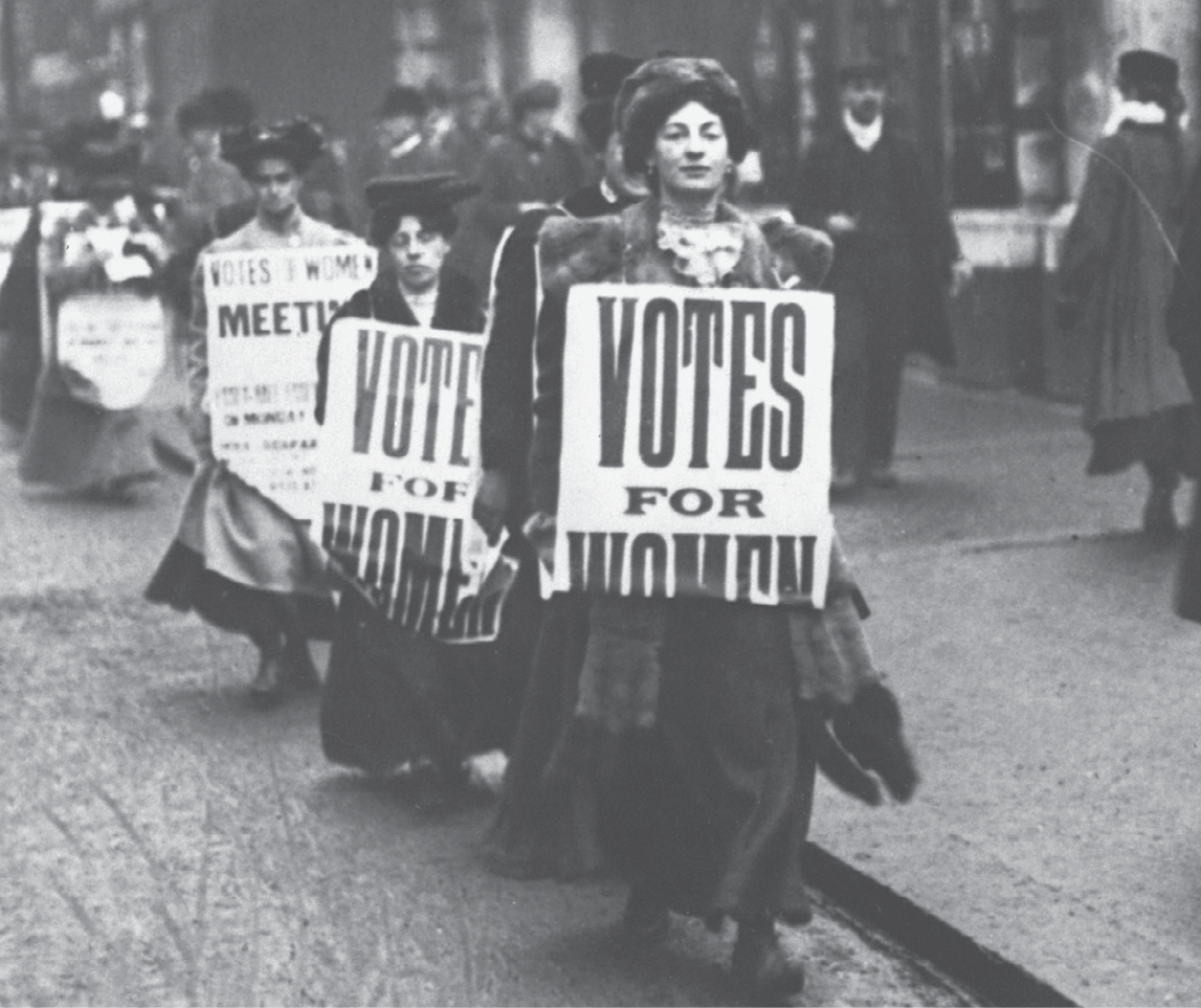 Fotografia. Imagem em preto e branco de mulheres em um protesto. Elas seguram cartazes com o texto: votes for women.