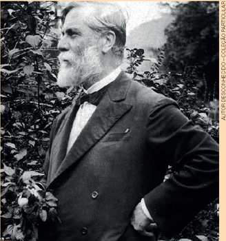 IMAGEM: fotografia antiga de um homem de lado, de barba e cabelos brancos, vestindo um paletó e gravata borboleta. FIM DA IMAGEM.