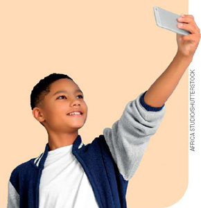 IMAGEM: um menino com o braço esticado para cima, segurando um celular na horizontal e sorrindo para ele. FIM DA IMAGEM.