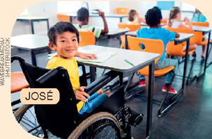 IMAGEM: um menino em uma cadeira de rodas atrás de uma mesa em uma sala de aula, com caderno e lápis apoiados em cima da mesa. FIM DA IMAGEM.