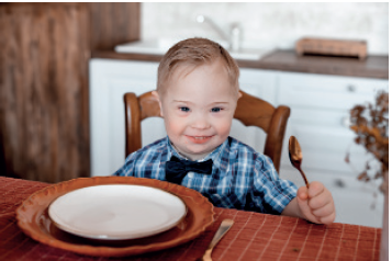IMAGEM: um menininho sentado à mesa segurando uma colher, com um prato vazio à sua frente. FIM DA IMAGEM.