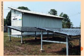 IMAGEM: painéis solares instalados em uma estrutura próxima do chão, ao lado de uma construção como uma cabana. FIM DA IMAGEM.