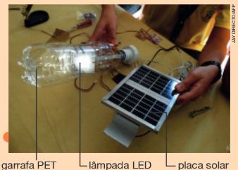IMAGEM: uma pessoa segura, com uma das mãos, uma garrafa pet contendo uma lâmpada led. na outra mão, uma placa solar. FIM DA IMAGEM.