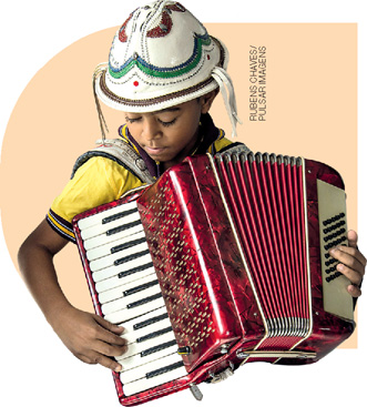 IMAGEM: menino tocando um acordeão. ele usa chapéu tradicional da cultural nordestina. FIM DA IMAGEM.