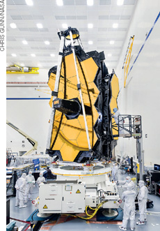 IMAGEM: em um laboratório, cinco cientistas vestidos em trajes de contenção, montam um telescópio espacial. FIM DA IMAGEM.