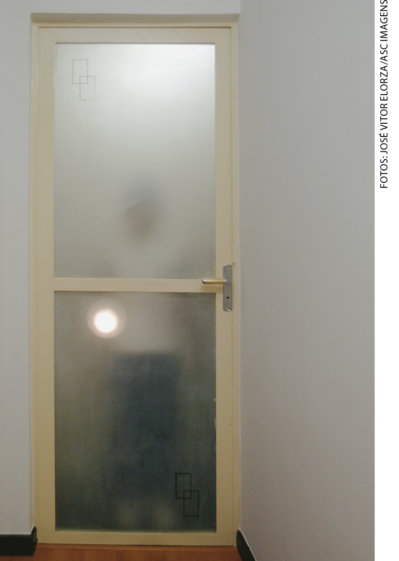 IMAGEM: silhueta de um menino atrás de uma porta de vidro fosco. apenas a luz da lanterna pode ser vista, bem mais fraca do que na imagem anterior. FIM DA IMAGEM.