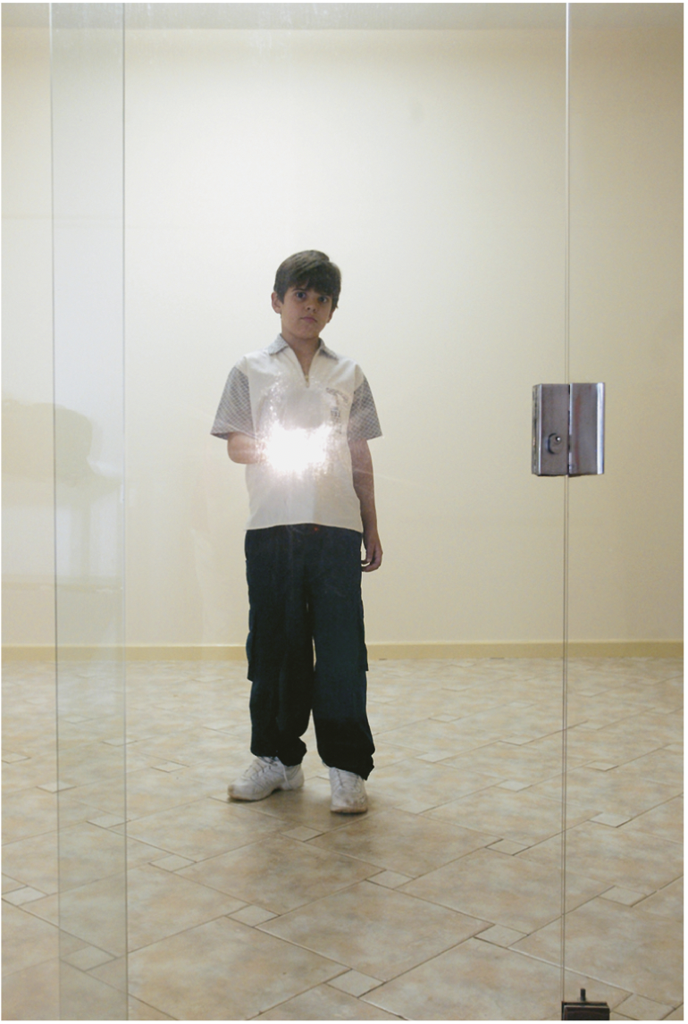 IMAGEM: um menino segura uma lanterna atrás de uma porta de vidro transparente. FIM DA IMAGEM.