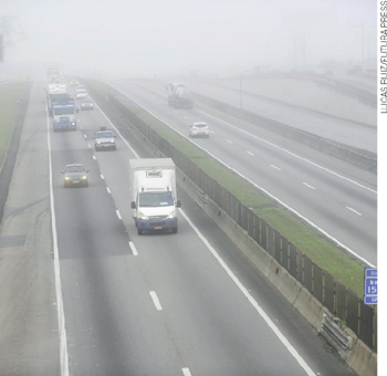 IMAGEM: rodovia coberta por neblina por onde trafegam carros e caminhões. FIM DA IMAGEM.