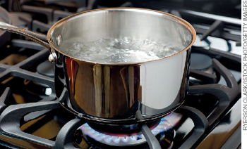 IMAGEM: panela sobre um fogão ligado contendo em seu interior água em ebulição. FIM DA IMAGEM.