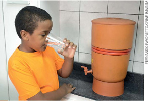 IMAGEM: garotinho bebendo água de um filtro de cerâmica. FIM DA IMAGEM.