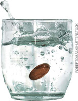 IMAGEM: uma moeda jogada em um copo com água, espirrando o líquido ao redor. FIM DA IMAGEM.