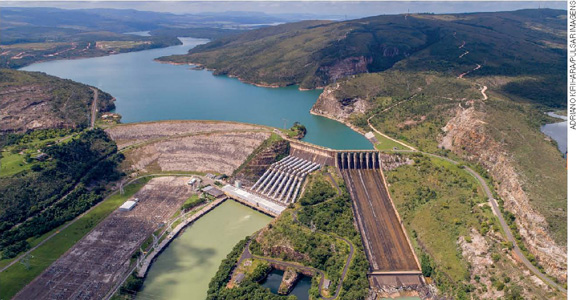 IMAGEM: vista aérea de uma usina hidrelétrica. ao fundo, estão a represa e a barragem, mais à frente, as tubulações que transportam a água até as turbinas. FIM DA IMAGEM.
