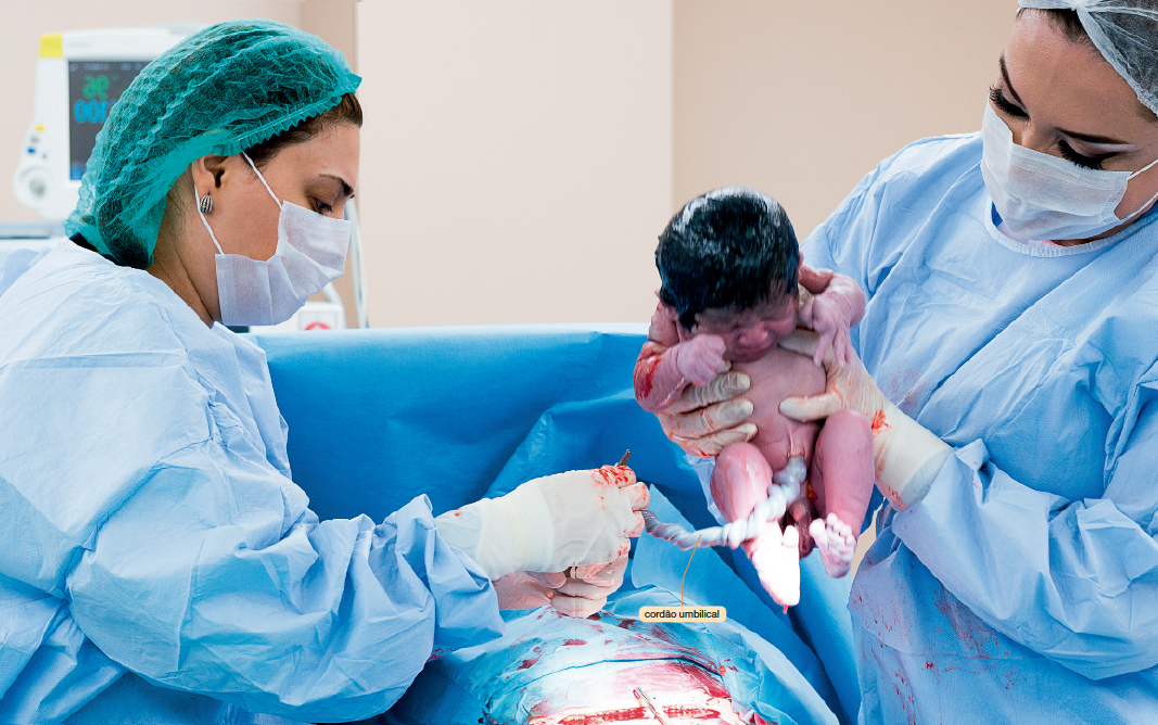 IMAGEM: Introdução da unidade 1. Profissionais da saúde durante a realização de um parto. Uma mulher segura o bebê recém-nascido enquanto outra corta o cordão umbilical. FIM DA IMAGEM.
