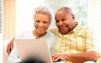 IMAGEM: um casal de idosos sorri para a tela de um computador. FIM DA IMAGEM.