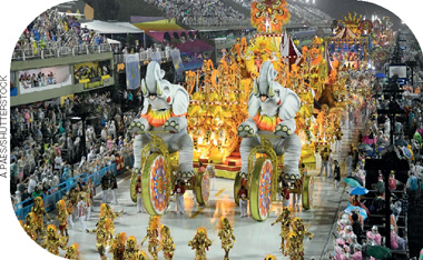 IMAGEM: fotografia de um desfile de escola de samba em uma avenida. centenas de componentes desfilam fantasiados. no centro, um carro grande e alto, traz as alegorias de dois elefantes à frente. arquibancadas ao lado estão lotadas de pessoas que assistem ao desfile. FIM DA IMAGEM.