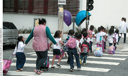 IMAGEM: crianças atravessam uma rua na faixa de pedestres ao lado de adultos. FIM DA IMAGEM.