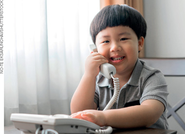 IMAGEM: um menino com traços asiáticos sorri ao atender um telefone. FIM DA IMAGEM.