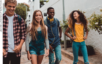 IMAGEM: quatro jovens usam roupas casuais, mochilas e sorriem andando em uma rua. FIM DA IMAGEM.