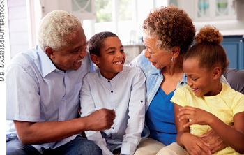 IMAGEM: um casal de idosos está sentado no sofá e ambos sorriem para os dois netos. FIM DA IMAGEM.