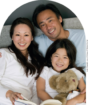IMAGEM: uma família asiática composta por um homem, uma mulher e uma criança sorriem sentados no sofá. FIM DA IMAGEM.