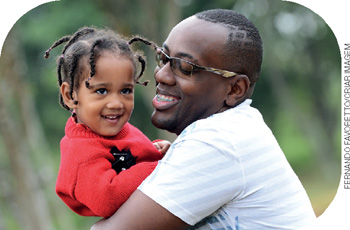 IMAGEM: um homem negro sorri e abraça uma menina negra pequena com tranças no cabelo. FIM DA IMAGEM.