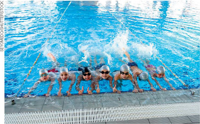 IMAGEM: sete crianças em uma piscina olímpica. elas usam óculos e toucas de natação. FIM DA IMAGEM.