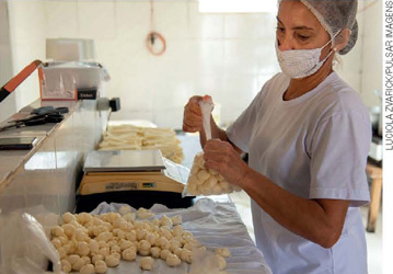 IMAGEM: mulher coloca queijos em formato de bolinhas em embalagens plásticas. FIM DA IMAGEM.