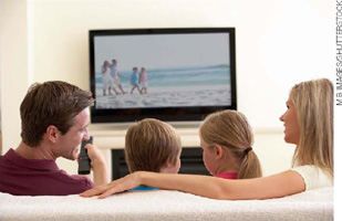 IMAGEM: um homem, duas crianças e uma mulher assistindo à televisão. FIM DA IMAGEM.