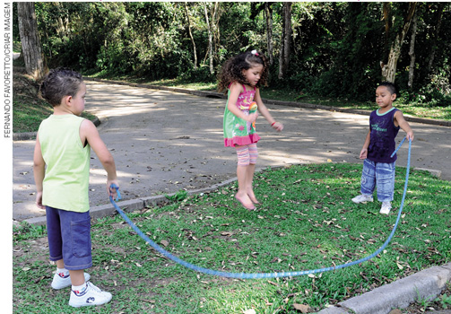 IMAGEM: três crianças brincam ao ar livre. dois garotos batem uma corda, enquanto uma garota pula. FIM DA IMAGEM.