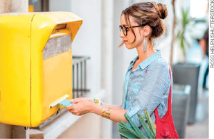 IMAGEM: mulher inserindo um envelope em uma caixa de correio. FIM DA IMAGEM.