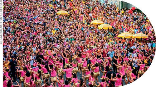 IMAGEM: muitas pessoas com camisetas coloridas, aglomeradas, dançam na rua. FIM DA IMAGEM.