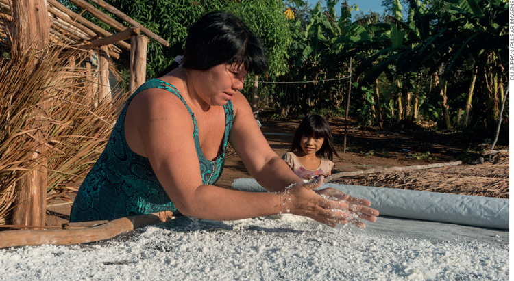 IMAGEM: uma mulher espalha uma farinha branca grossa sobre uma superfície plana. FIM DA IMAGEM.