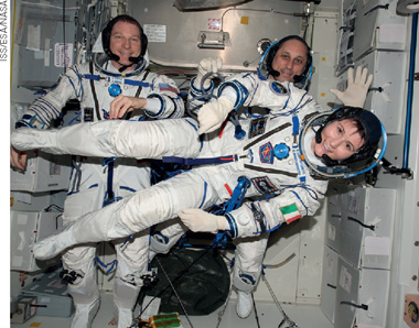 IMAGEM: três astronautas flutuam com seus macacões e equipamentos. FIM DA IMAGEM.