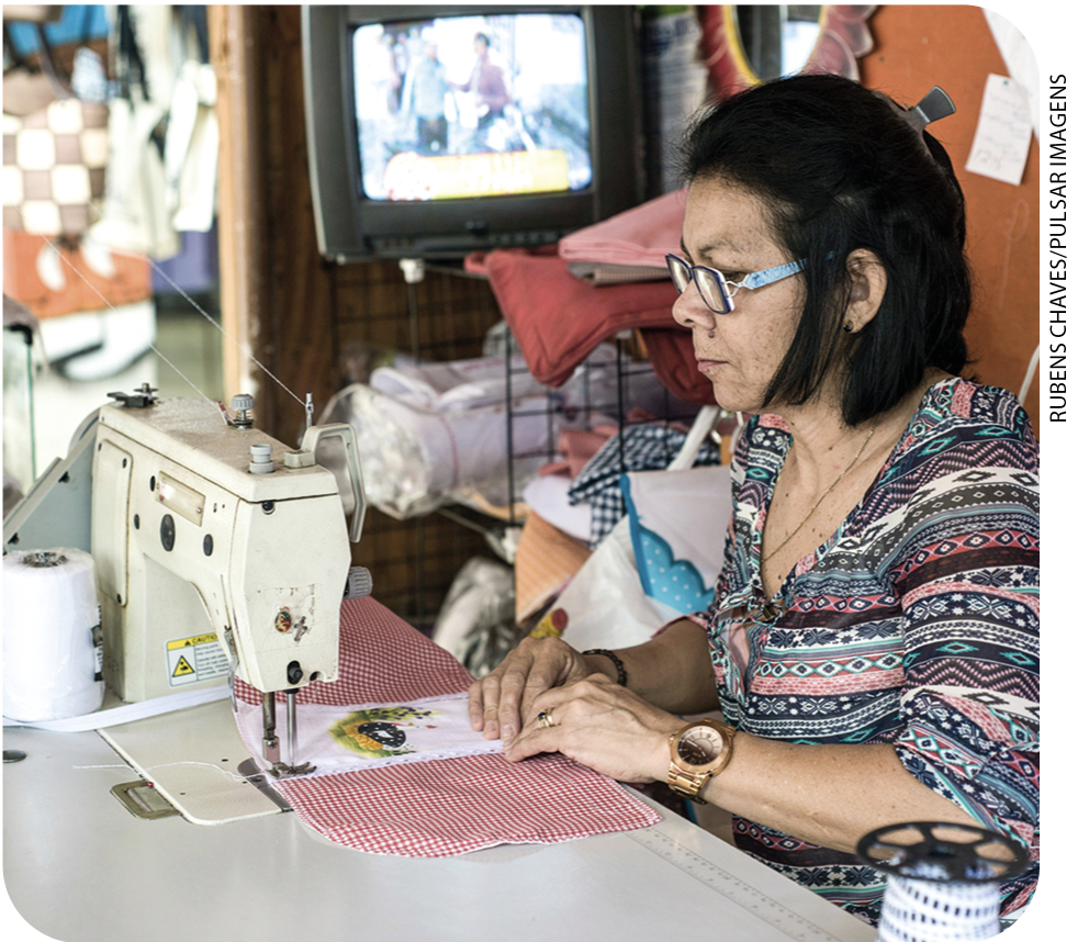 IMAGEM: uma mulher usa uma máquina elétrica para costurar um tecido. FIM DA IMAGEM.