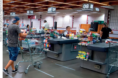 IMAGEM: em caixas de supermercado, funcionários atendem às pessoas com suas compras. FIM DA IMAGEM.
