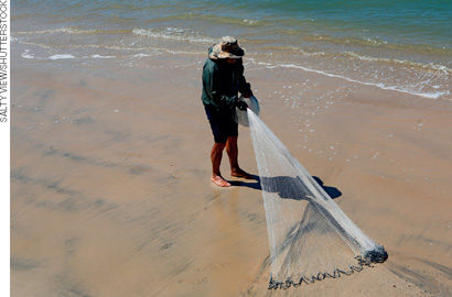 IMAGEM: um homem arrasta uma rede de pesca à beira do mar. FIM DA IMAGEM.