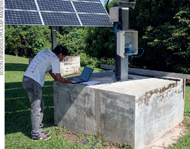IMAGEM: um homem usa um computador em uma estação com painéis de captação de energia solar. FIM DA IMAGEM.