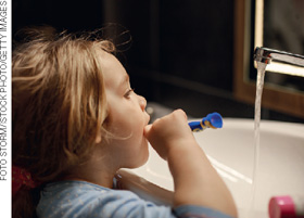 IMAGEM: uma menina escova os dentes com a torneira aberta. FIM DA IMAGEM.