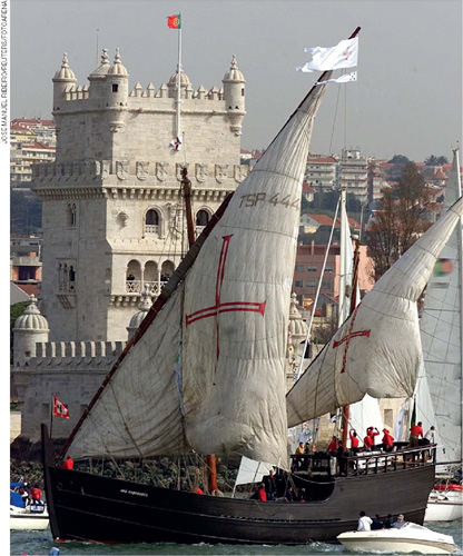 IMAGEM: no mar, uma antiga embarcação à vela e sua tripulação. ao fundo, a torre de um castelo com a bandeira de portugal hasteada. FIM DA IMAGEM.