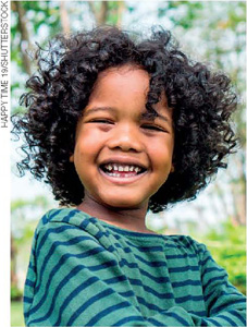 IMAGEM: uma criança negra com cabelo encaracolado sorri para uma foto. FIM DA IMAGEM.