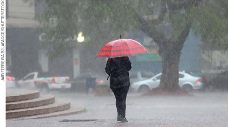IMAGEM: uma pessoa de costas caminha com um guarda-chuva aberto debaixo de forte chuva. FIM DA IMAGEM.