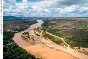 IMAGEM: fotografia aérea de um rio com as águas turvas de lama e sedimentos. a margem da direita possui uma faixa de terra sem vegetação que se estende para o meio do rio, bifurcando-se em bancos de areia. FIM DA IMAGEM.