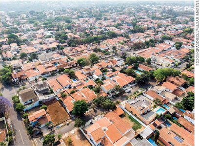 IMAGEM: vista aérea de telhados de casas construídas em quarteirões, em um bairro residencial. as ruas são asfaltadas e há algumas árvores. FIM DA IMAGEM.
