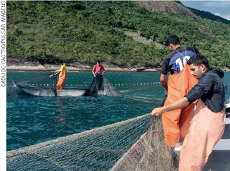 IMAGEM: pescadores em barcos pequenos lançam redes de pesca ao mar. FIM DA IMAGEM.