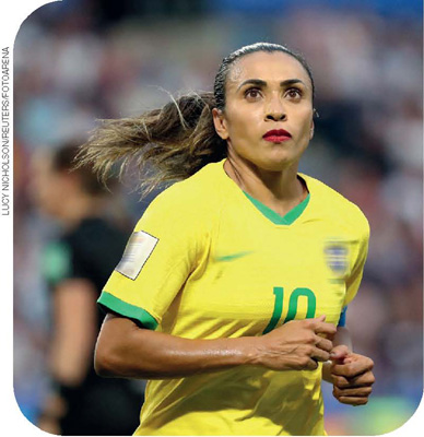 IMAGEM: uma foto de meio-corpo mostra a jogadora de futebol marta. ela olha acima e à frente e está correndo. usa rabo de cavalo e batom, e veste a camisa da seleção brasileira de futebol feminino. FIM DA IMAGEM.