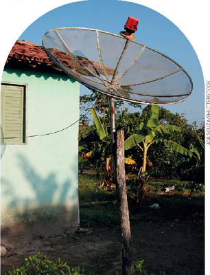 IMAGEM: em um terreno gramado, uma antena parabólica de onde sai um cabo ligado a uma casa pequena. FIM DA IMAGEM.