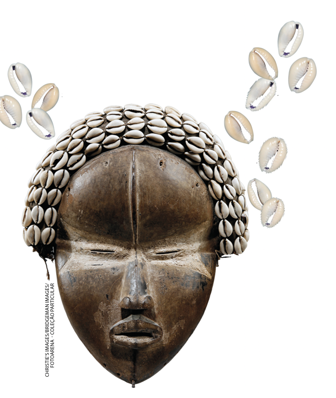 IMAGEM: item c. artefato em madeira, representando um rosto com olhos puxados. pequenas conchas adornam o contorno da cabeça. FIM DA IMAGEM.
