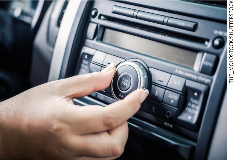 IMAGEM: item a. fotografia de uma mão ajustando o aparelho de rádio instalado em um console de carro. FIM DA IMAGEM.