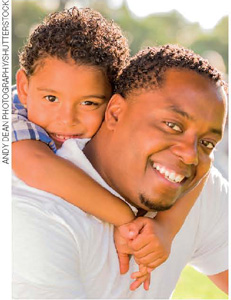 IMAGEM: um homem e um menino negros sorriem para a foto. a criança abraça seu pescoço. FIM DA IMAGEM.