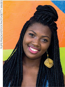 IMAGEM: uma jovem negra com cabelo longo e trançado olha para a foto e sorri. FIM DA IMAGEM.